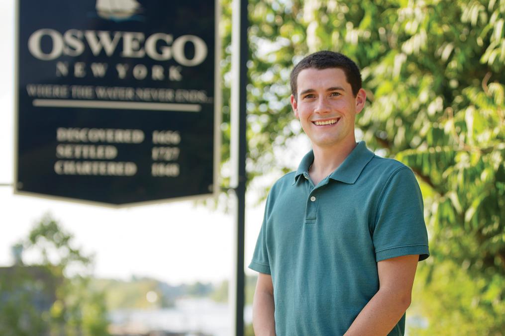 Tom Drumm '15 stands in front of an Oswego, New York sign. Tom represents Oswego in the County Legislature. 