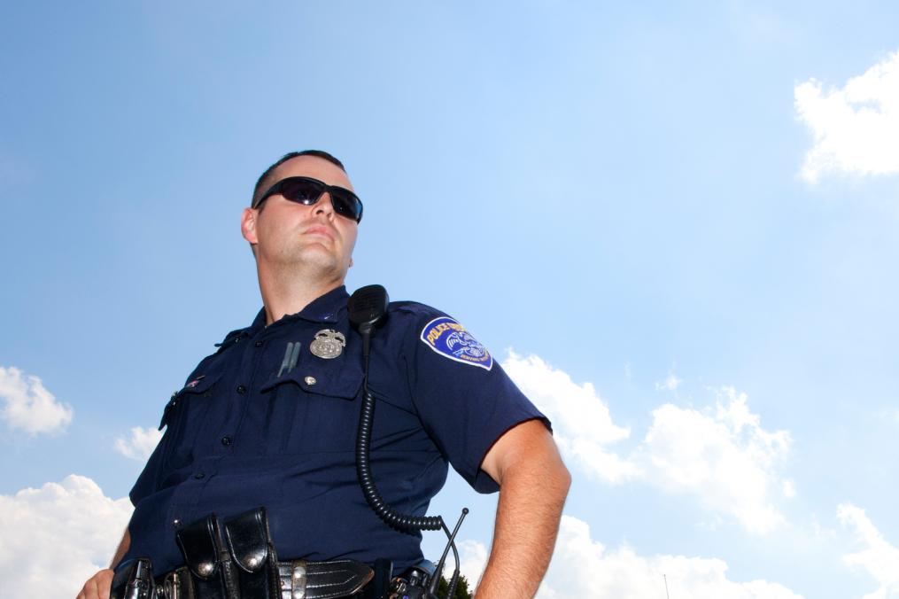 A police officer stands next to his car. Studies show that police officers with a Criminal Justice degree are happier in their positions.