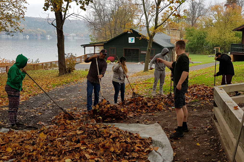 students raking leaves in a backyard with a lakeview