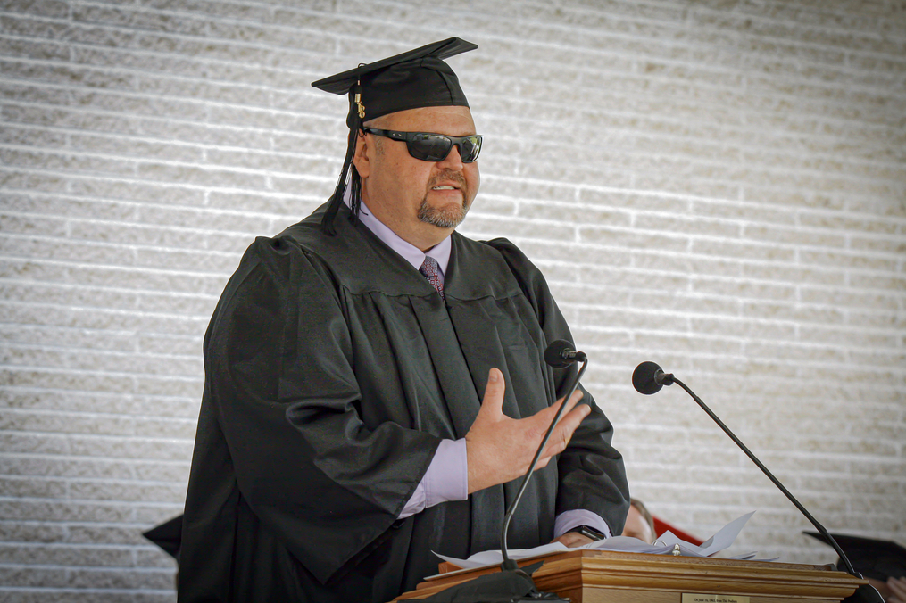 Guy in his cap and gown speaking at a podium at graduation