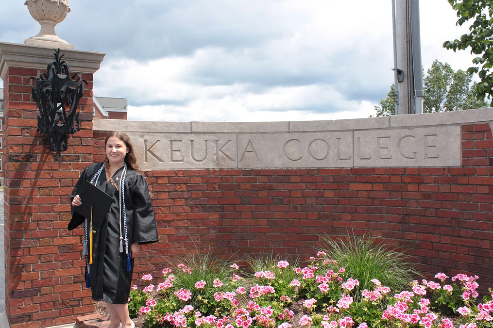 Maddie Roberts standing in front of the Keuka College entrance wall in her gradation gown