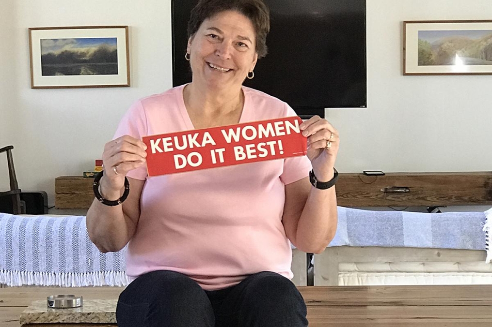 Libby Stearns Faison '73 holding a bumper sticker that says "Keuka Women Do It Best!"