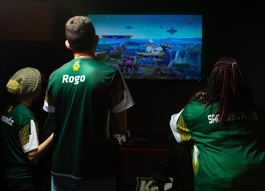Three students gather around an esports screen