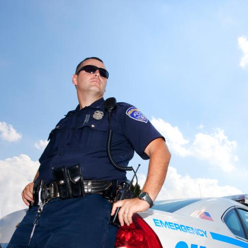 A police officer stands next to his car. Studies show that police officers with a Criminal Justice degree are happier in their positions.