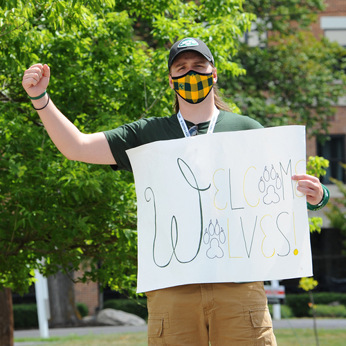 student wearing a mask holding a "welcome wolves" sign